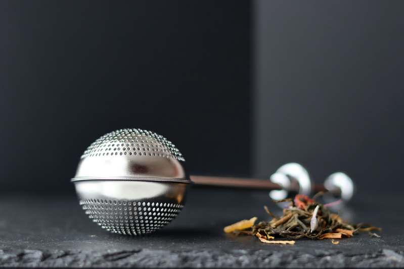 Two hands holding a glass teapot with a stainless steel infuser inside, sunlight streaming through kitchen window